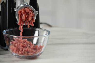 Electric meat grinder with beef mince on white table against blurred background, closeup. Space for text