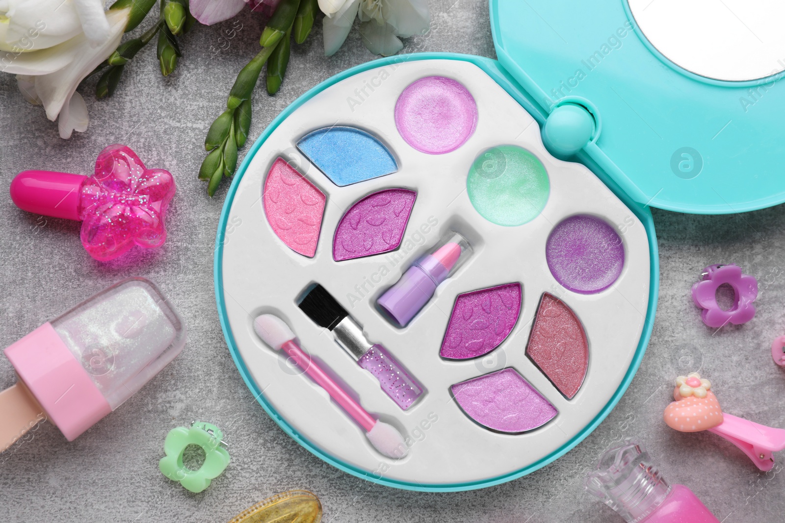 Photo of Decorative cosmetics for kids. Eye shadow palette, lipsticks, accessories and flowers on grey table, flat lay