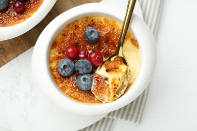 Delicious creme brulee with berries and mint in bowl on white table, top view