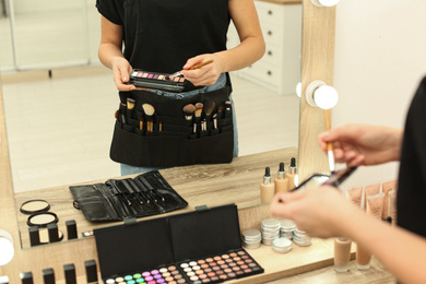 Photo of Professional makeup artist with eyeshadow palette and belt organizer full of tools in studio, closeup