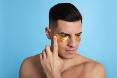 Photo of Man applying golden under eye patch on light blue background
