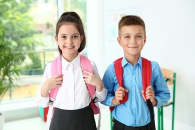 Photo of Cute little children with backpacks in classroom at school