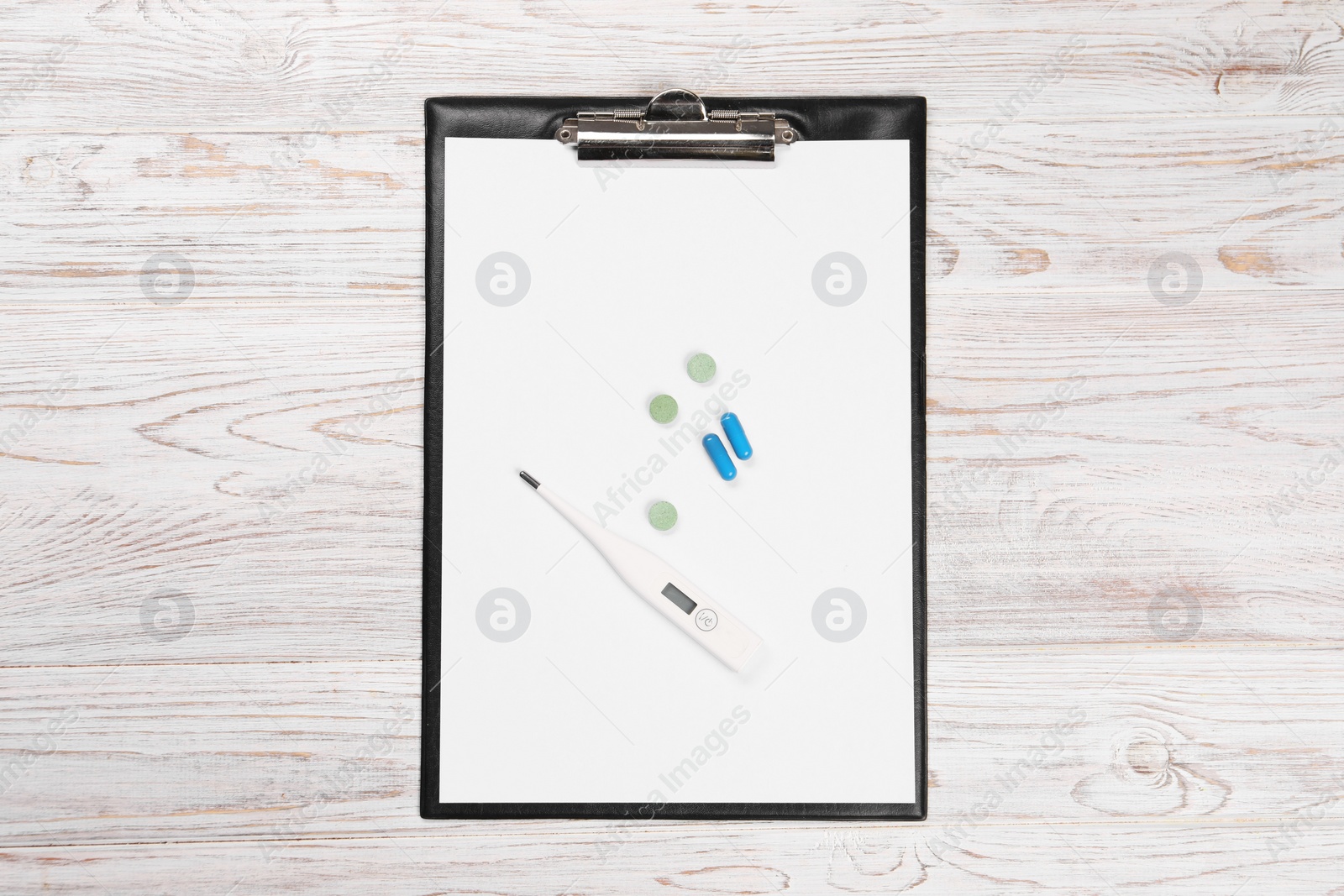 Photo of Clipboard, thermometer and pills on wooden table, top view