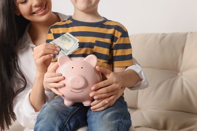 Photo of Mother and her son putting money into piggy bank at home, closeup