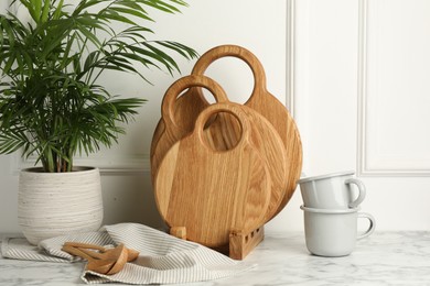 Photo of Wooden cutting boards, spoons, dishware and houseplant on white marble table