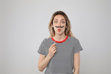 Emotional woman with fake mustache on grey background