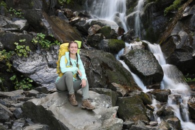 Happy tourist with backpack resting near mountain waterfall
