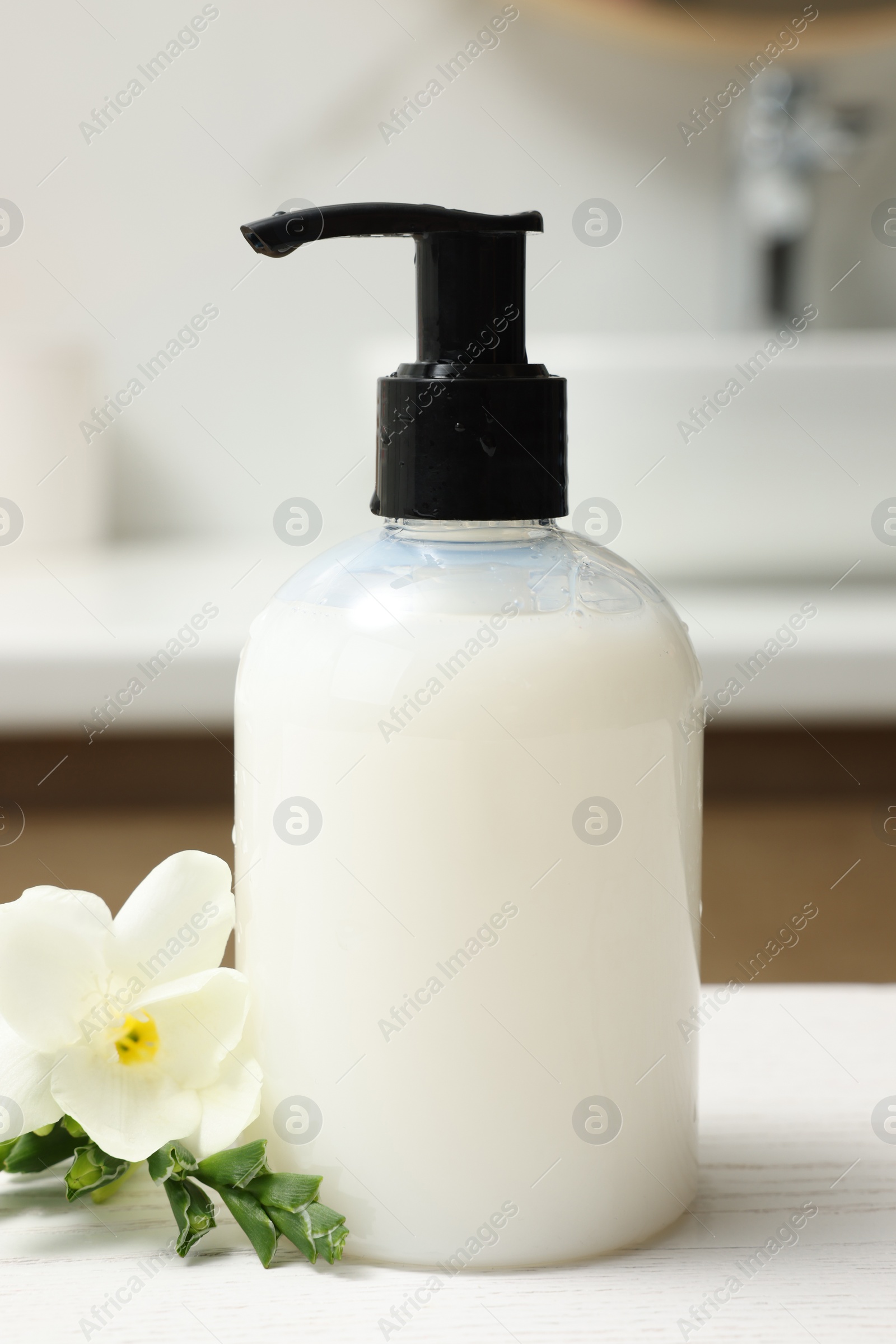 Photo of Dispenser of liquid soap and freesia flower on white table in bathroom