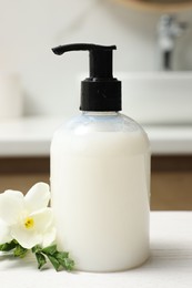 Dispenser of liquid soap and freesia flower on white table in bathroom