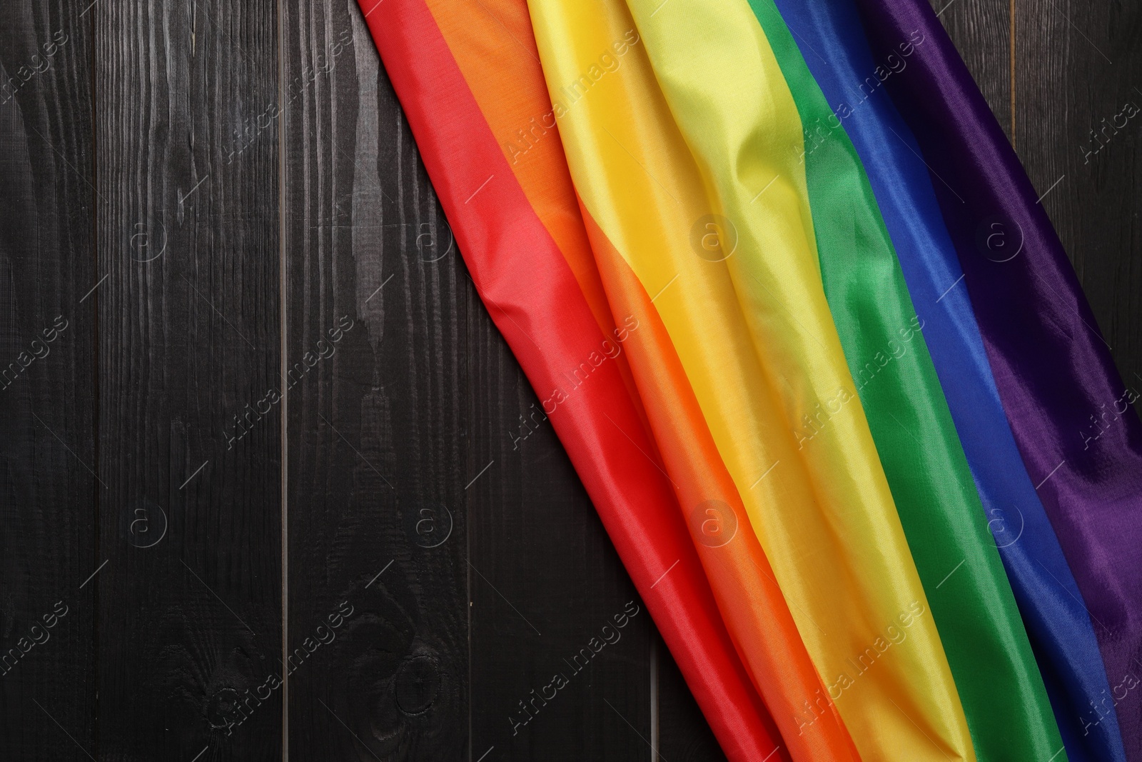 Photo of Rainbow LGBT flag on black wooden background, top view. Space for text