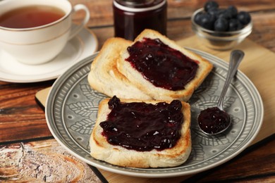 Photo of Delicious toasts with blueberry jam and cup of tea on wooden table