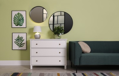 White chest of drawers with lamp, sofa and mirrors on wall in living room. Interior design