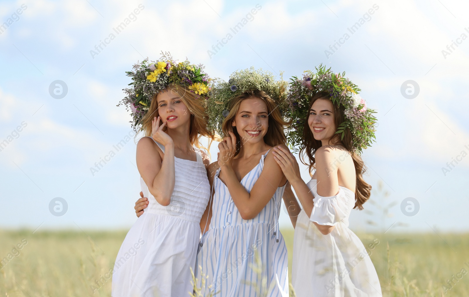 Photo of Young women wearing wreaths made of beautiful flowers in field on sunny day