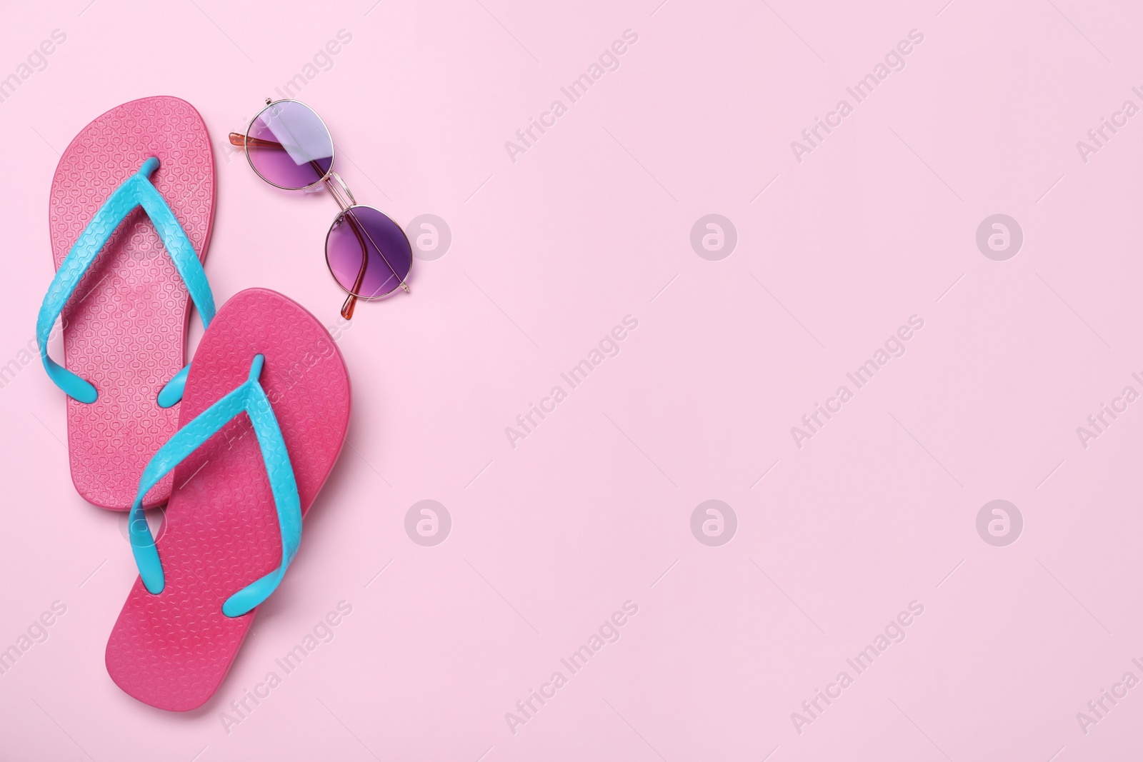 Photo of Stylish flip flops and sunglasses on pink background, flat lay. Space for text