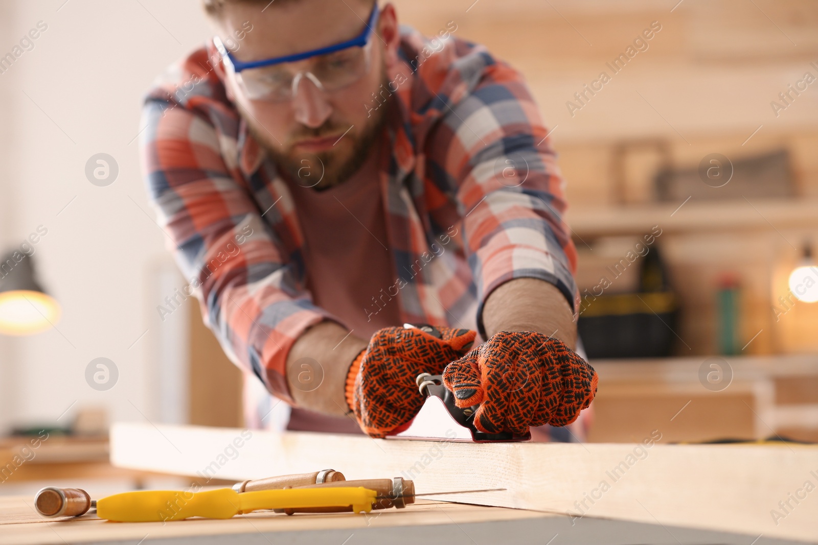 Photo of Carpenter shaping wooden bar with plane at table in workshop, focus on hands