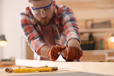 Carpenter shaping wooden bar with plane at table in workshop, focus on hands