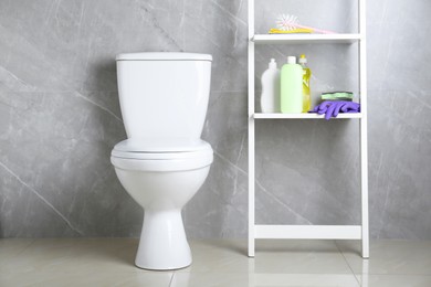 Photo of Toilet bowl and shelving unit with cleaning supplies indoors