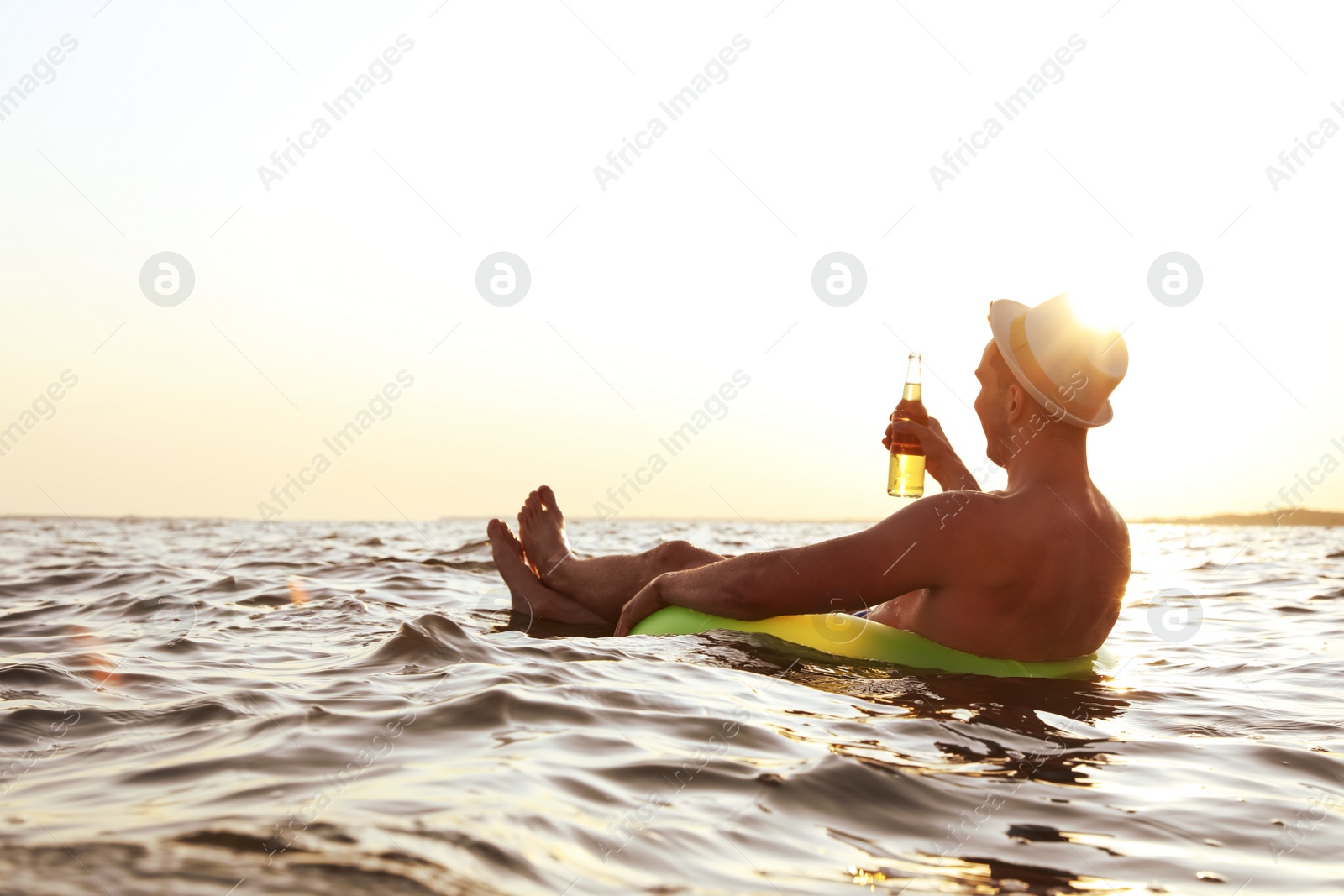 Photo of Young man with drink on inflatable ring in sea