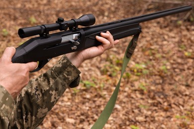 Photo of Man with hunting rifle wearing camouflage outdoors, closeup