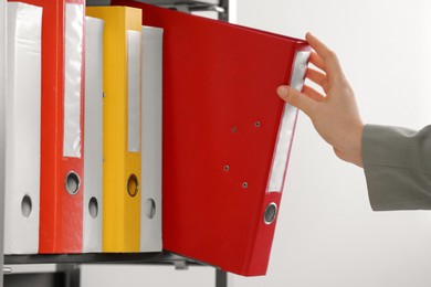 Woman taking folder with documents from shelf on white background, closeup