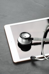 Photo of Modern tablet and stethoscope on black table, closeup