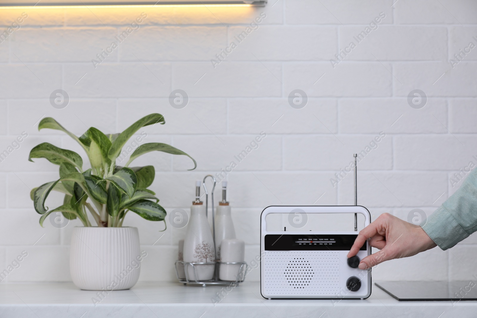 Photo of Woman turning volume knob on radio in kitchen, closeup