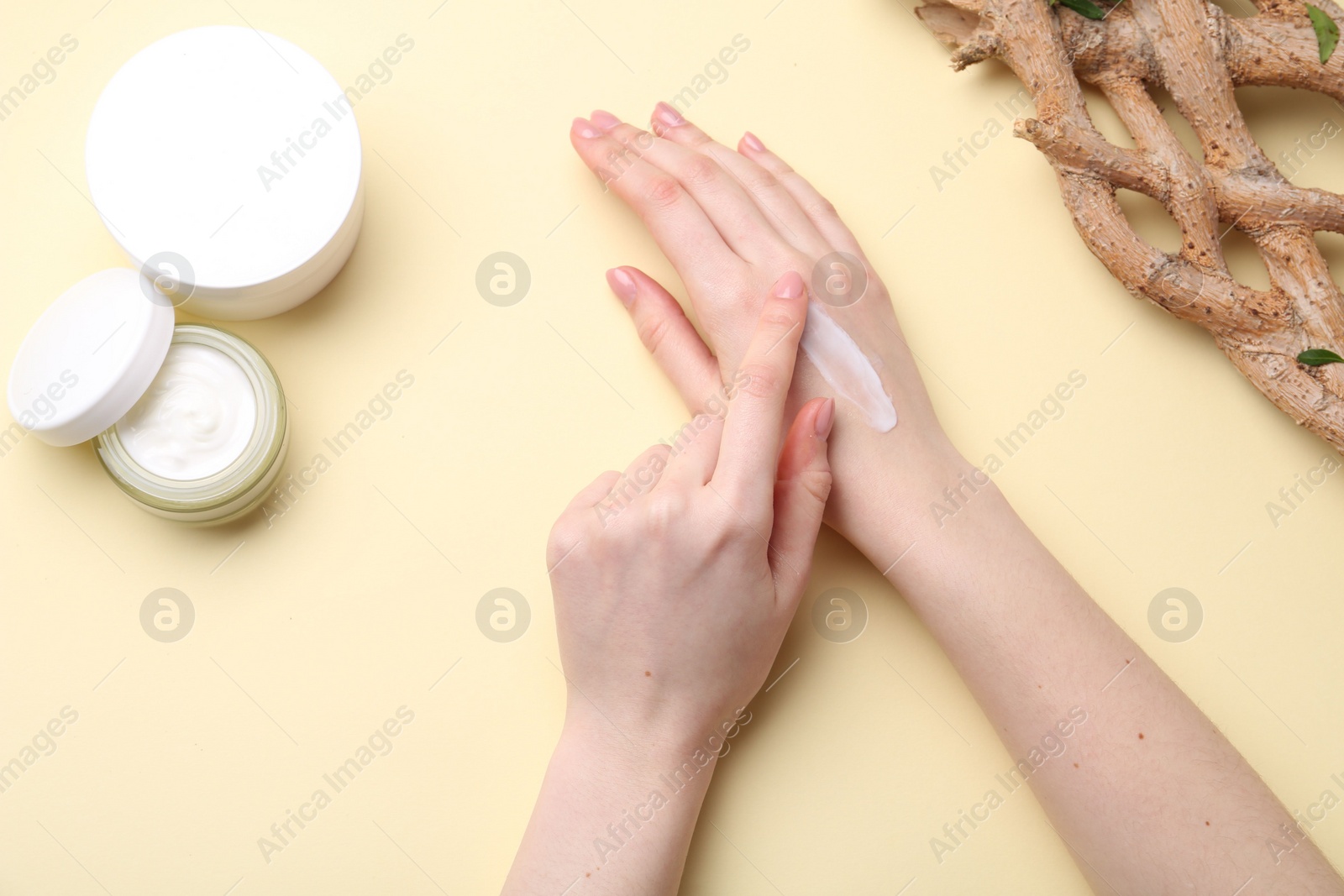 Photo of Woman applying hand cream on beige background, top view