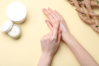 Woman applying hand cream on beige background, top view