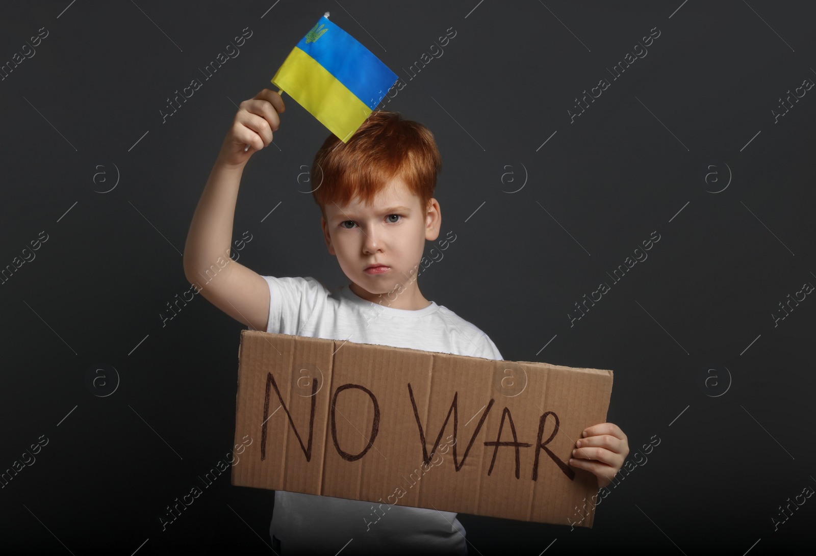 Photo of Boy holding poster No War and Ukrainian flag against black background