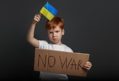 Boy holding poster No War and Ukrainian flag against black background