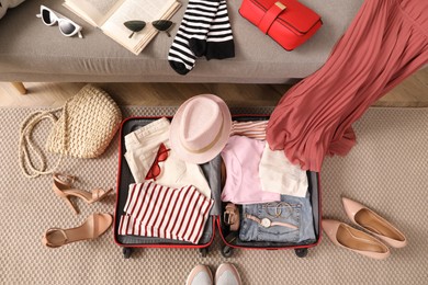 Photo of Open suitcase with different women clothes and accessories on floor, top view