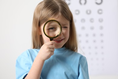 Photo of Little girl with magnifying glass against vision test chart