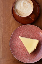 Photo of Cup of coffee and slice of cheesecake on wooden table, top view