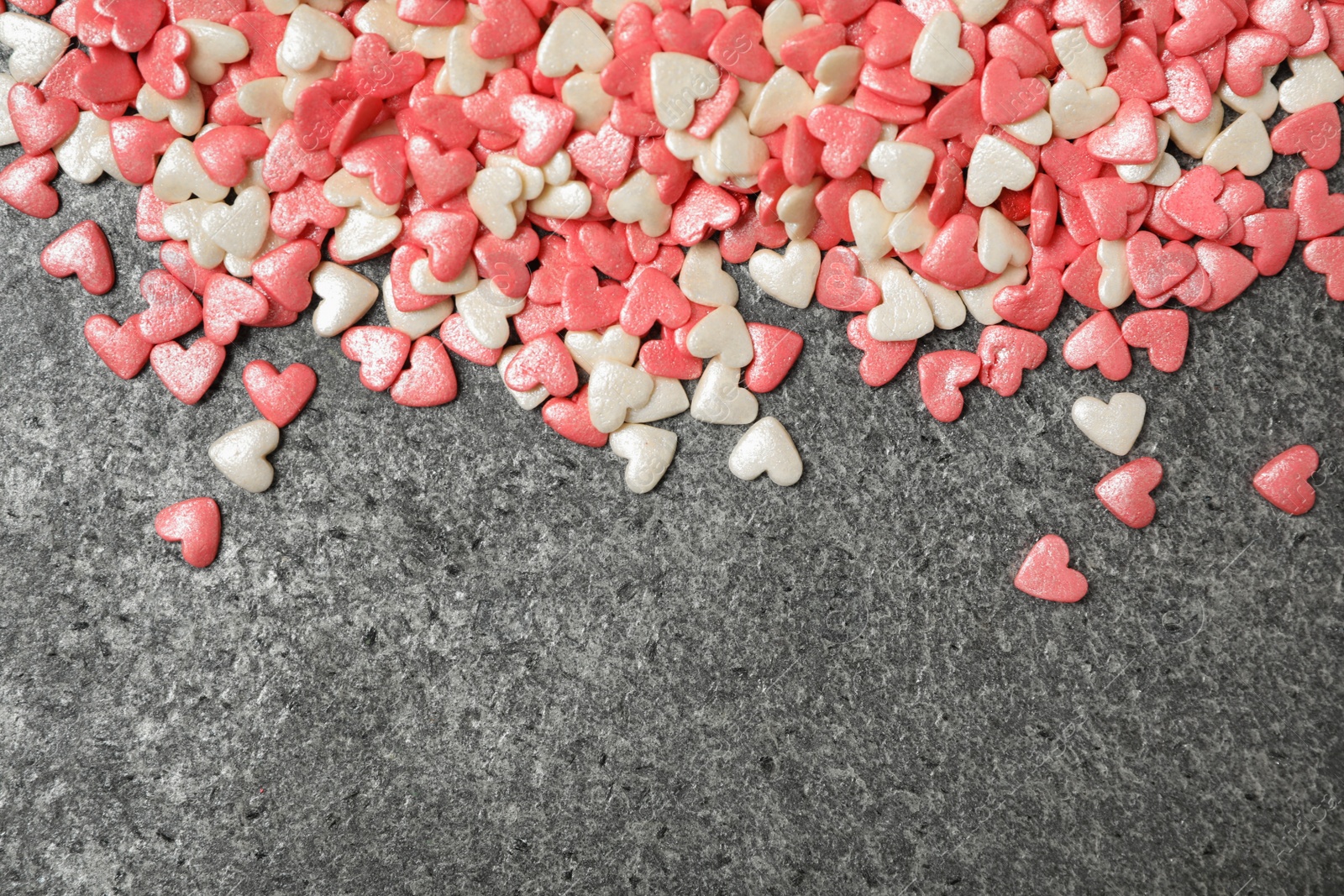 Photo of Bright heart shaped sprinkles on grey table, flat lay. Space for text