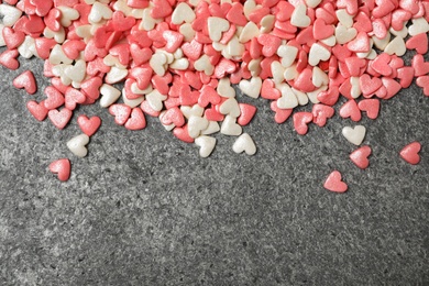 Bright heart shaped sprinkles on grey table, flat lay. Space for text