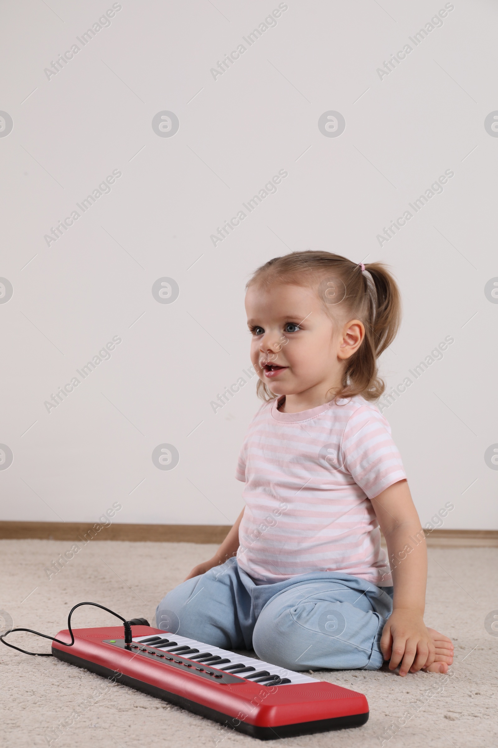 Photo of Cute little girl playing with toy piano at home