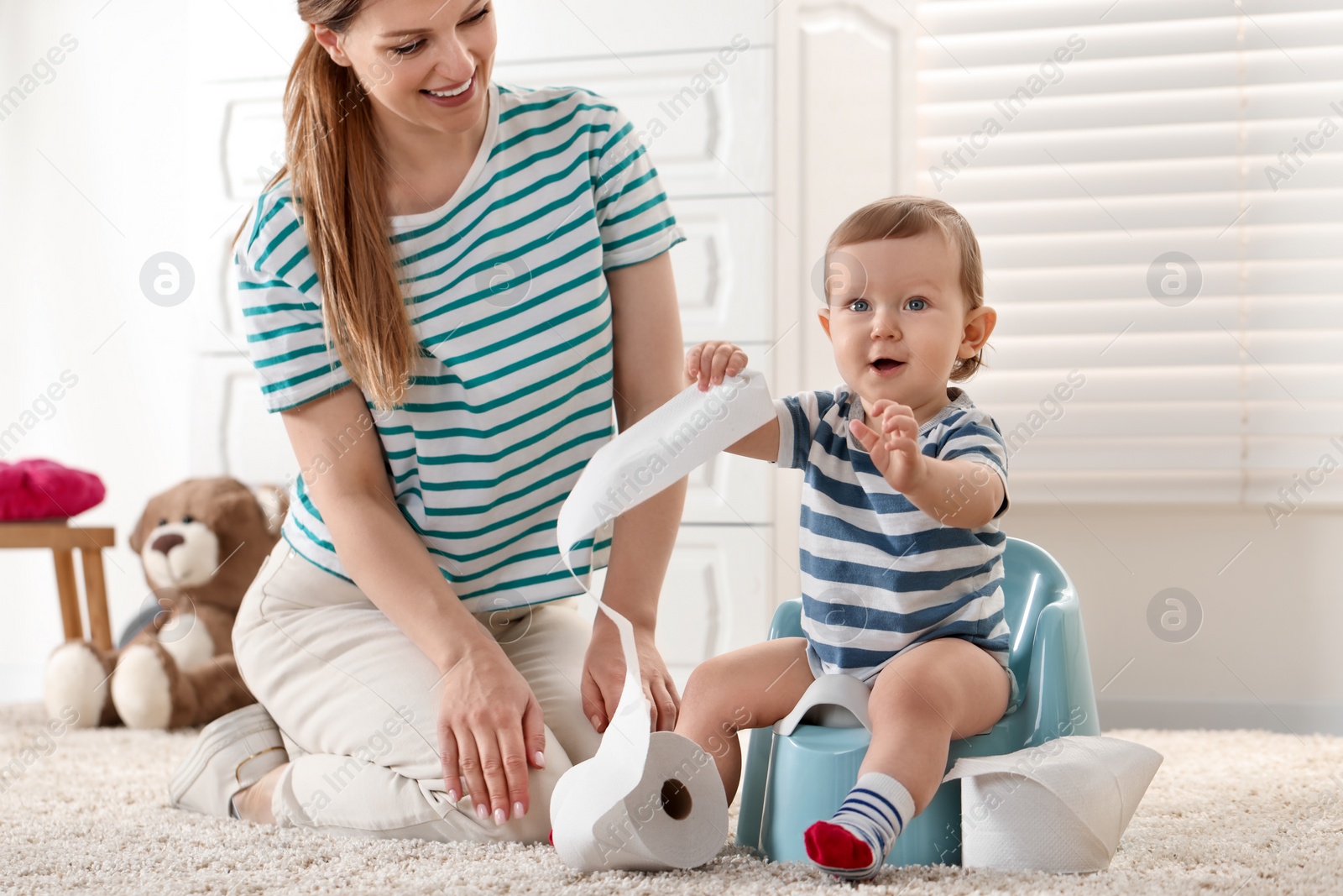 Photo of Mother training her child to sit on baby potty indoors