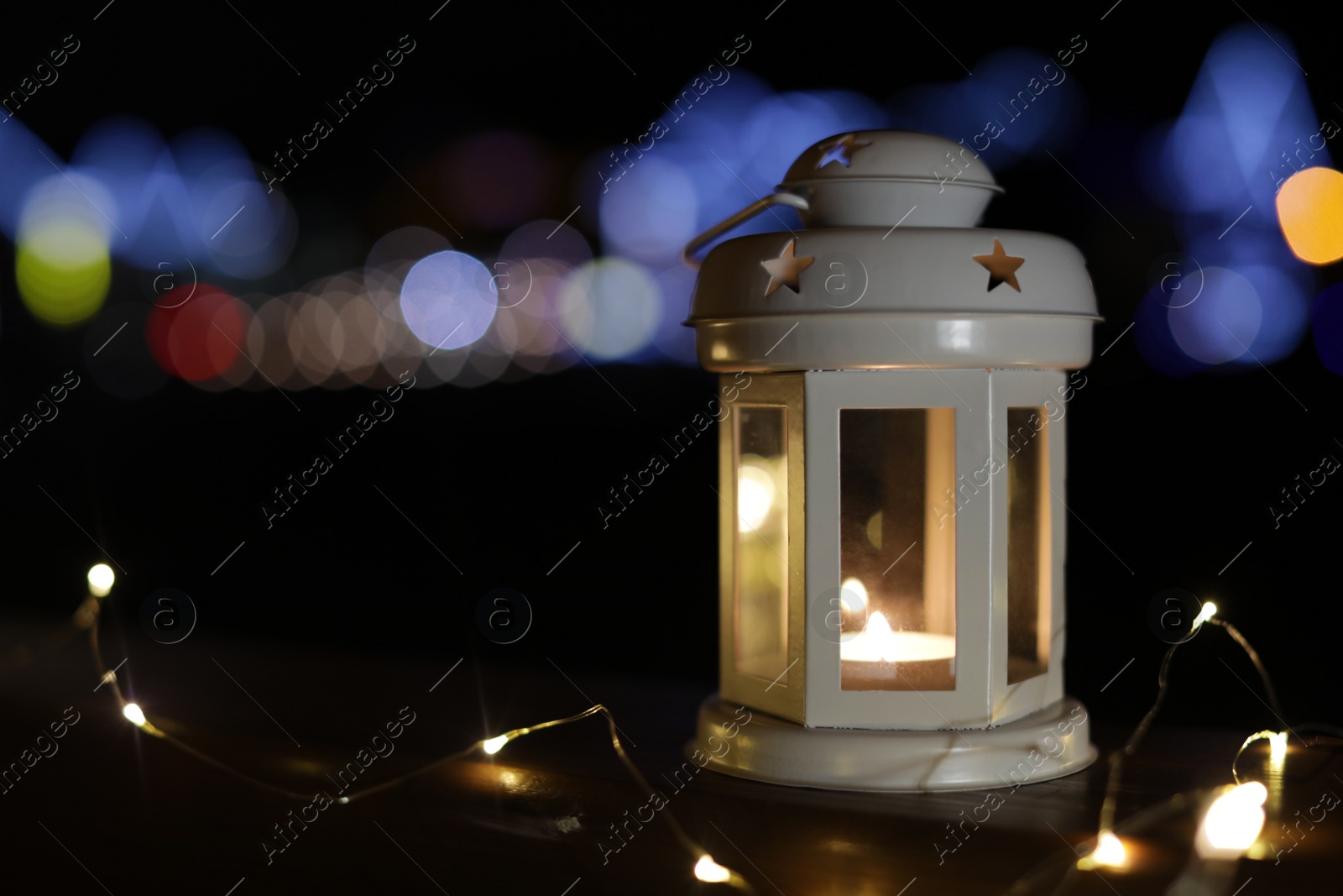 Photo of Lantern and Christmas lights on wooden railing outdoors against blurred background, space for text. Winter night