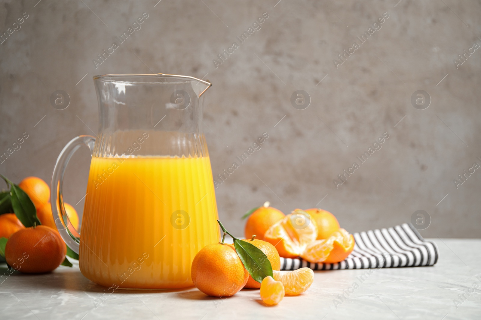 Photo of Jug of fresh tangerine juice and fruits on light table. Space for text