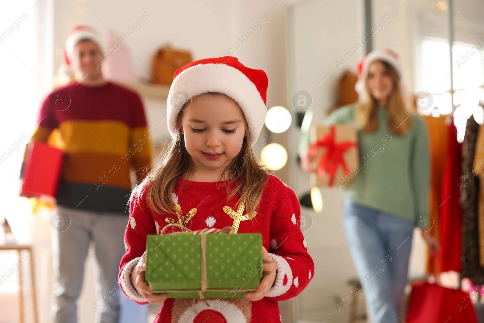 Photo of Little girl with gift box near her parents in store. Family Christmas shopping