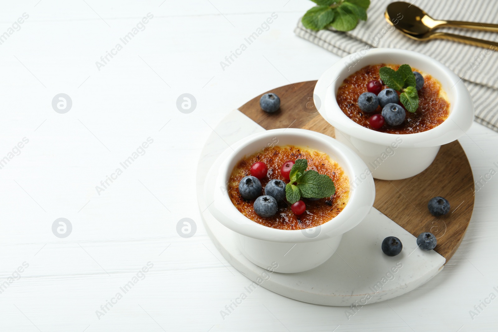 Photo of Delicious creme brulee with berries and mint in bowls on white wooden table. Space for text