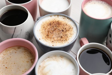 Many different cups with aromatic hot coffee on white wooden table, closeup