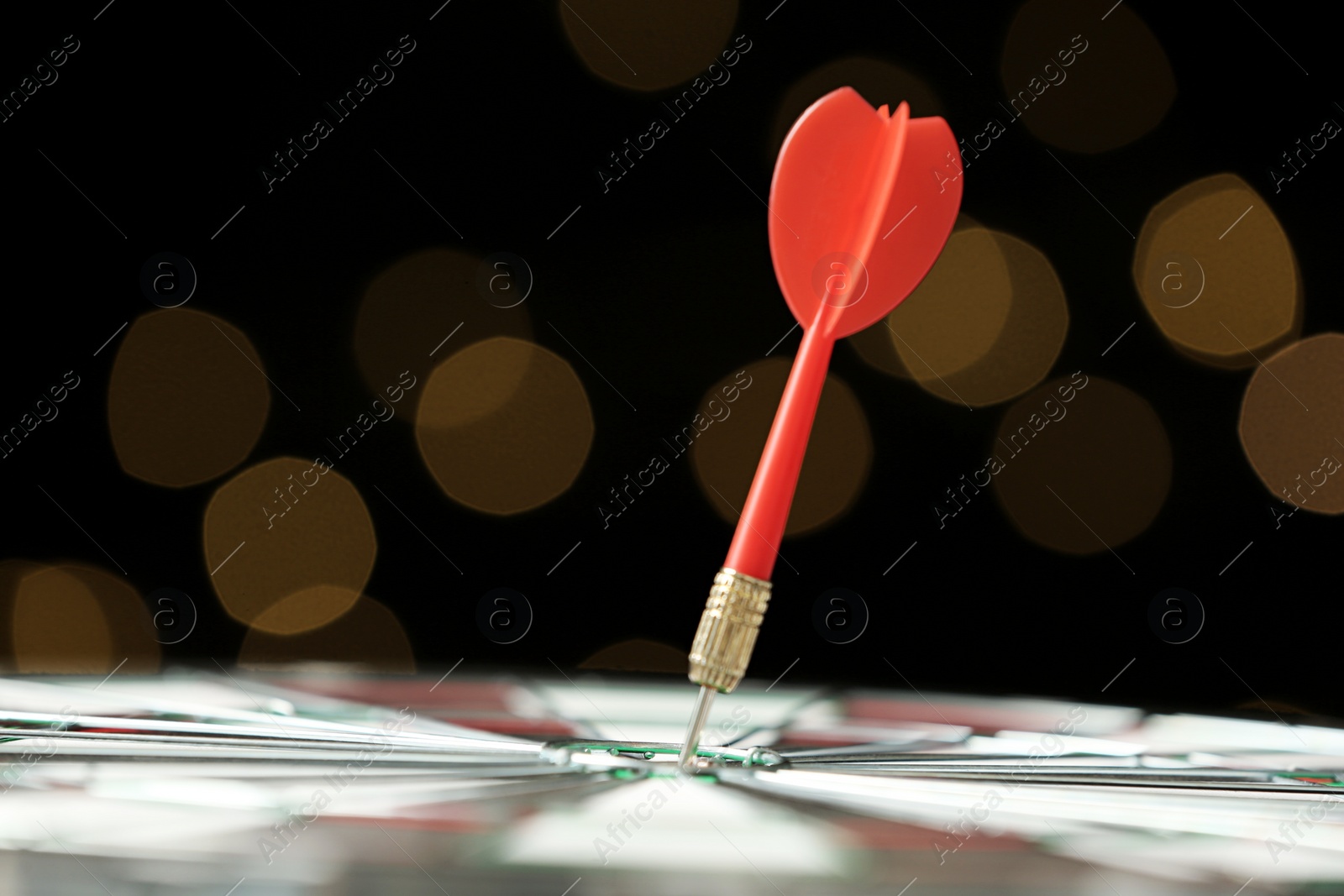 Photo of Red arrow hitting target on dart board against blurred lights