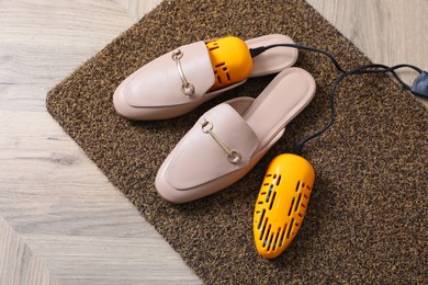 Pair of stylish shoes with modern electric footwear dryer on door mat indoors, above view