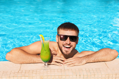Image of Young bearded man with refreshing cocktail in swimming pool at resort