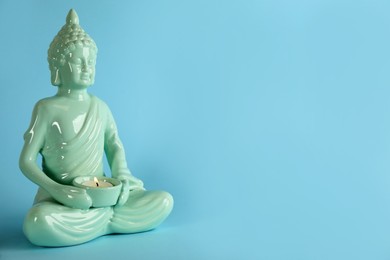 Photo of Beautiful ceramic Buddha sculpture with burning candle on light blue background. Space for text