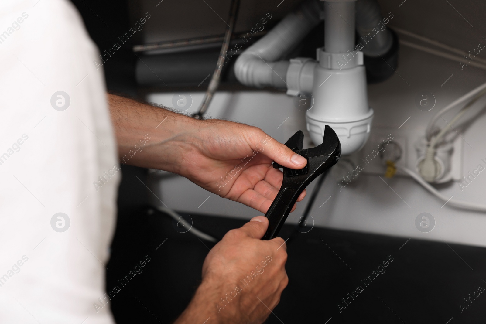 Photo of Professional plumber with adjustable wrench fixing sink, closeup