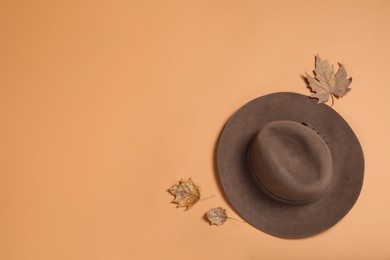Photo of Stylish hat and autumn leaves on orange background, flat lay. Space for text