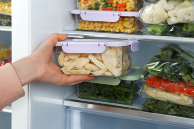 Photo of Woman taking container with frozen potato from refrigerator, closeup