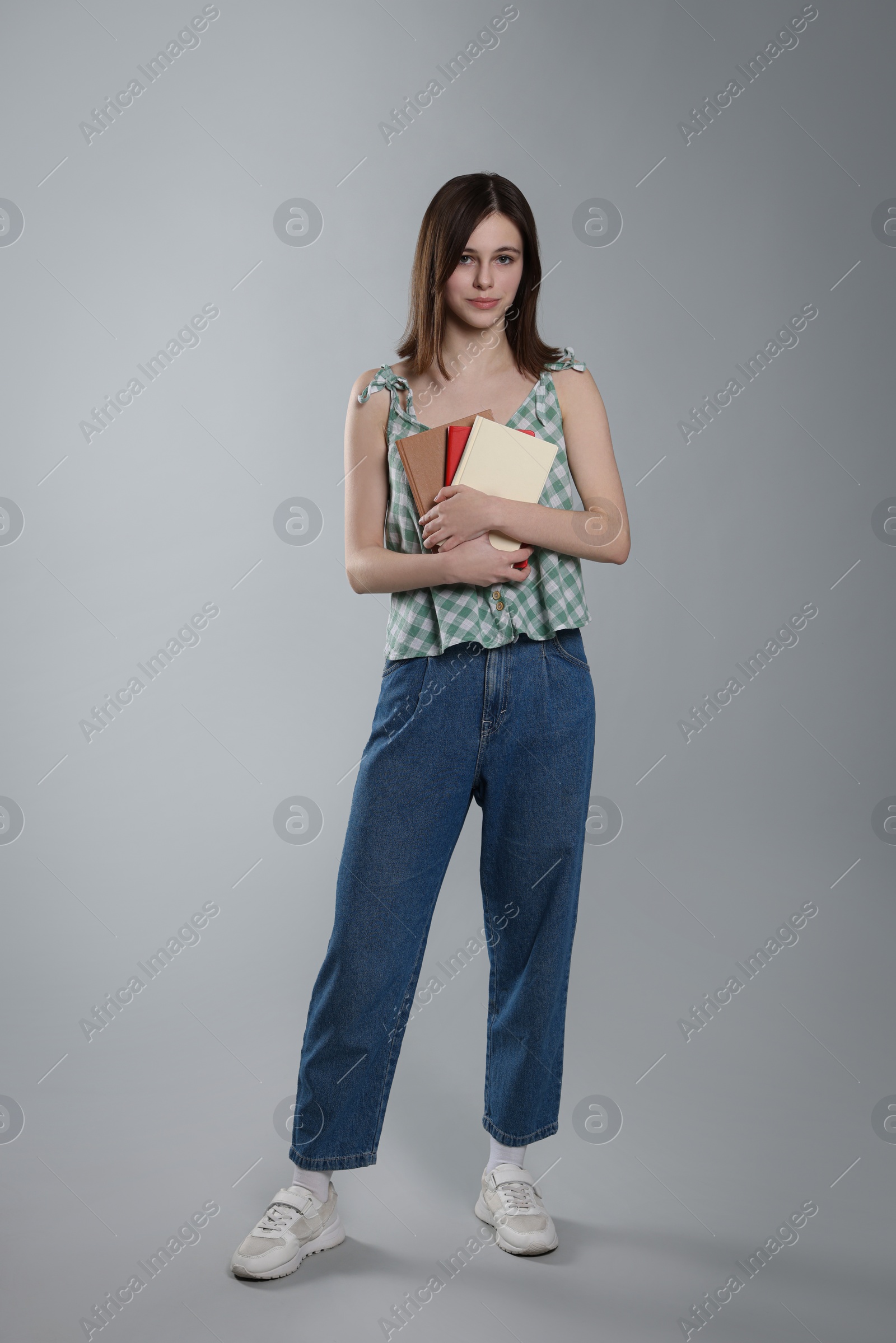 Photo of Cute teenage girl with books on light grey background